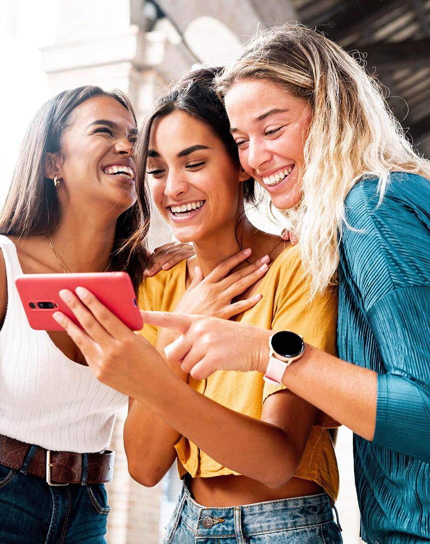 Drei junge Frauen schauen lachend auf ein Smartphone